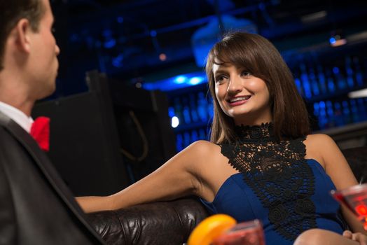 portrait of a woman in a nightclub, sitting on the couch and talking with man