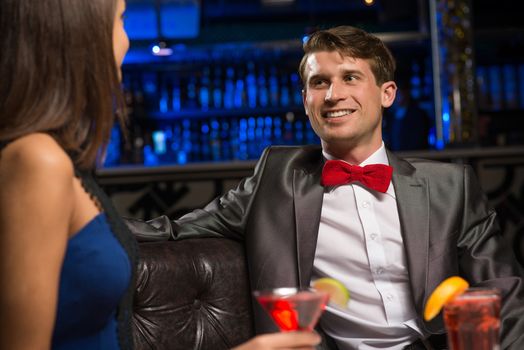 portrait of a man in a nightclub, sitting on the couch and talking with woman