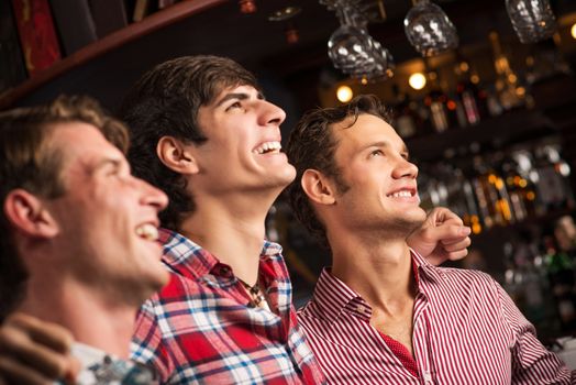 Three men stand in a row embracing smile and look in front of you, sports fans