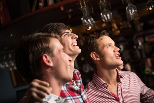 Three men stand in a row embracing smile and look in front of you, sports fans