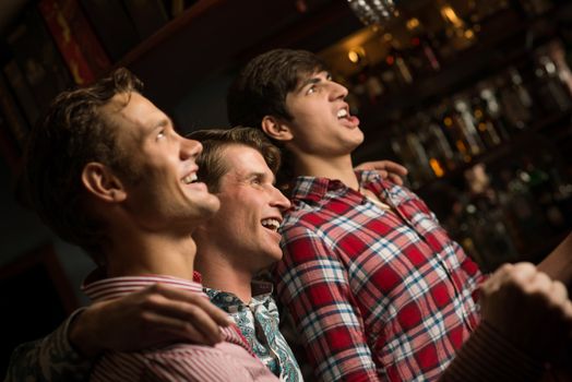 Three men stand in a row embracing smile and look in front of you, sports fans