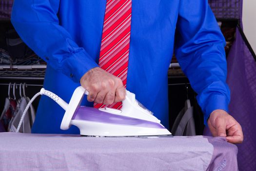 Businessman with red tie and blue shirt ironing shirt against wardrobe.