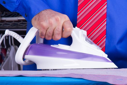 Businessman with red tie and blue shirt holding iron against wardrobe.