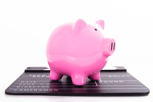Black film clapper board with pink piggy bank, isolated on white background.