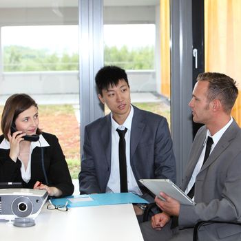 Business colleagues having a discussion seated close together at a table analysing a document with the woman talking on the phone while watching her two male coworkers