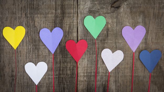 Several colorful paper hearts on wooden textured background