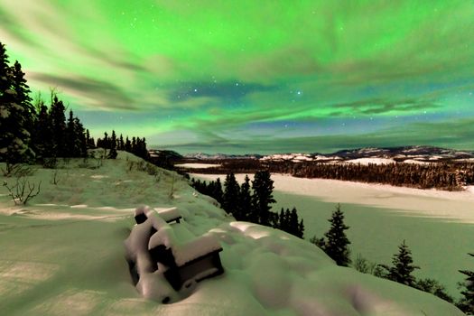 Spectacular view from snow-covered bench: light clouds and Northern Lights or Aurora borealis on night sky over snowy winter landscape of Lake Laberge Yukon Territory Canada