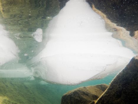 Underwater shot of ice floes floating in clear shallow water with rocky bottom mirrored on water surface
