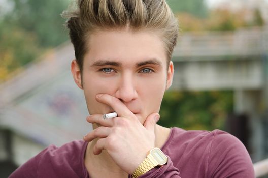 Attractive blue eyed, blond young man smoking cigarette outdoors
