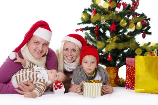 Happy family with two children in Santa hats under Christmas tree over white