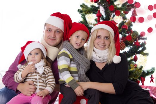 Happy family with two children in Santa hats under Christmas tree over white