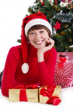 Smiling woman in red Santa hat lying under Christmas tree with gifts