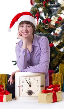 Smiling woman with clock under Christmas tree on white