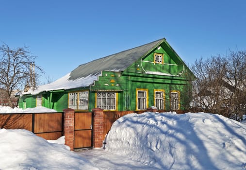 Old green wooden house between snowdrifts, winter sunny day