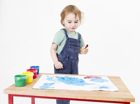 child behind small desk with blue painting. studio shot in grey background