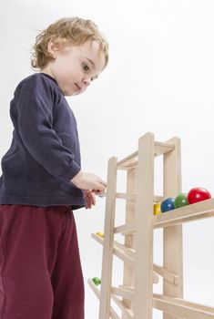 young child playing with wooden ball path. studio shot in grey background