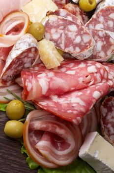 Delicatessen Cold Cuts with Smoked Ham, Pepperoni, Salami, Green Olives and Brie Cheese closeup on Dark Wooden background