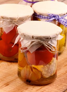 Arrangement of Mixed Pickled Vegetables in Glass Jars Covered with Butter-paper closeup on Wooden background