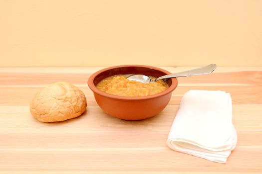 Spoon in a bowl of lentil soup with a bread roll and white napkin