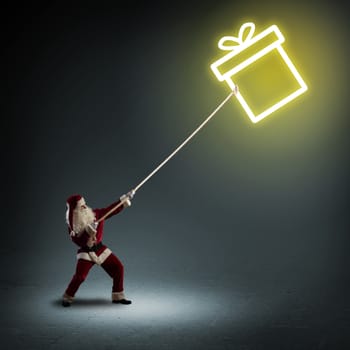 Santa Claus pulls a rope with a symbol box with a gift