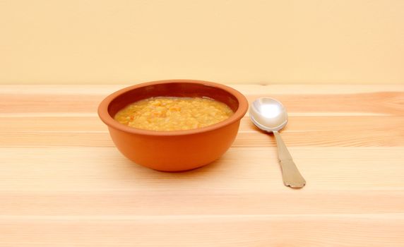 Bowl of vegetable soup with a spoon on a pine table with copy space