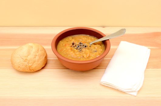 Lentil soup in a bowl with seasoning and bread roll, spoon and napkin
