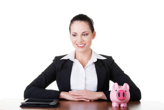 Businesswoman at the desk with tablet and piggy bank, isolated on white. Modern banking concept.