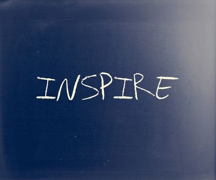 "Inspire" handwritten with white chalk on a blackboard.