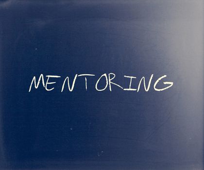 The word "Mentoring" handwritten with white chalk on a blackboard.