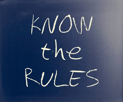 "Know the rules" handwritten with white chalk on a blackboard.