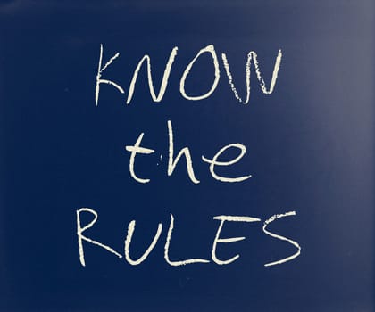 "Know the rules" handwritten with white chalk on a blackboard.