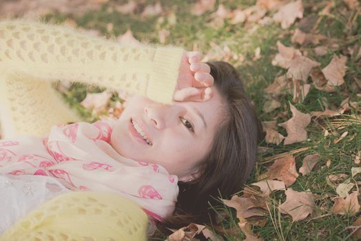 Young woman laying in grass with a bunch of fallen leafs, covering one eye