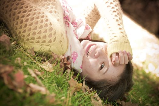 Young woman laying in grass with a bunch of fallen leafs, covering one eye