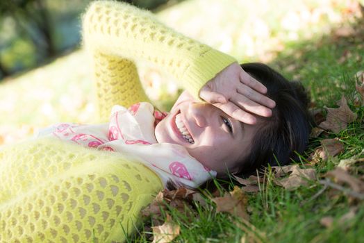 Young woman laying in grass with a bunch of fallen leafs, covering one eye