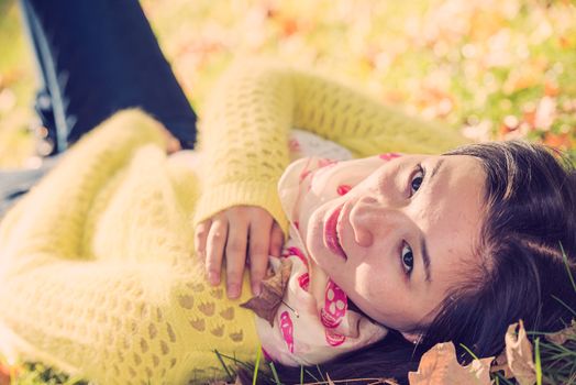 Young woman laying in grass with a bunch of fallen leafs