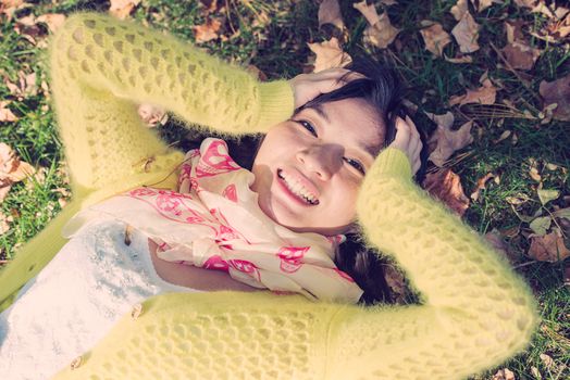 Young woman laying in grass with a bunch of fallen leafs, holding her head