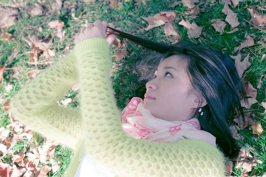 Young woman laying in grass with a bunch of fallen leafs, pulling her hair