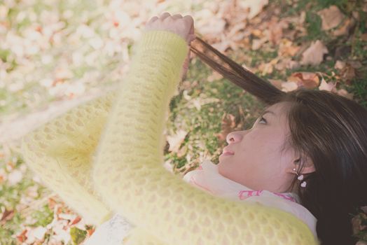 Young woman laying in grass with a bunch of fallen leafs, pulling her hair