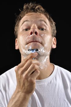 Portrait of Caucasian man shaving chin with sharp razor on black background