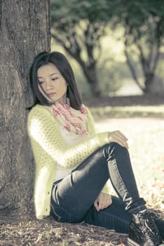 Portrait of lonely young woman sitting against a tree looking upset