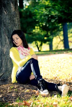 Portrait of lonely young woman sitting against a tree looking upset