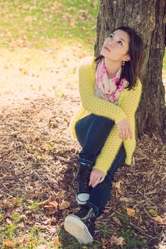 Portrait of happy looking woman sitting against a tree and looking upwards