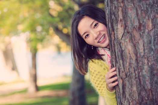 portrait of shy young woman peaking from behind a tree and smiling