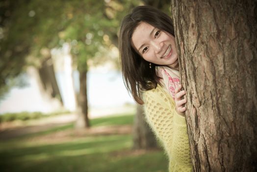 portrait of shy young woman peaking from behind a tree and smiling