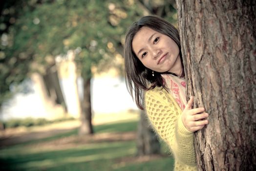 portrait of shy young woman peaking from behind a tree and smiling