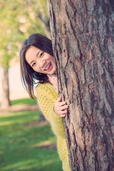 portrait of shy young woman peaking from behind a tree and sticking out her tougue