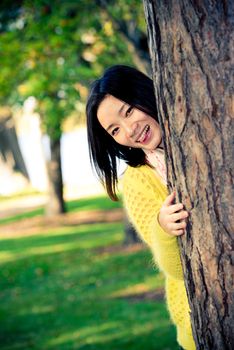 portrait of shy young woman peaking from behind a tree and sticking out her tougue