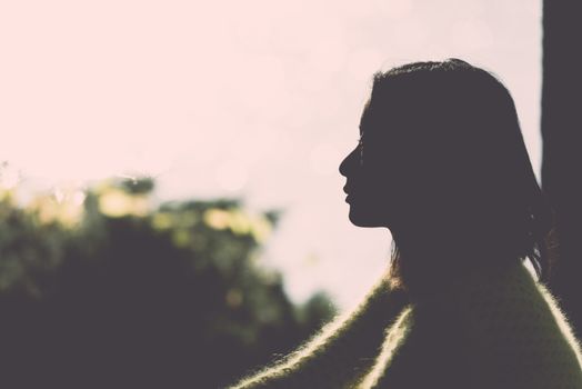 Silhouette portrait of lonely young woman sitting during dusk time