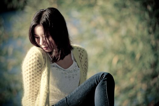 Attractive lonely young woman sitting on a rock next to river looking upset