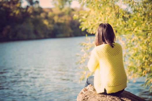 Attractive lonely young woman sitting on a rock next to river looking upset